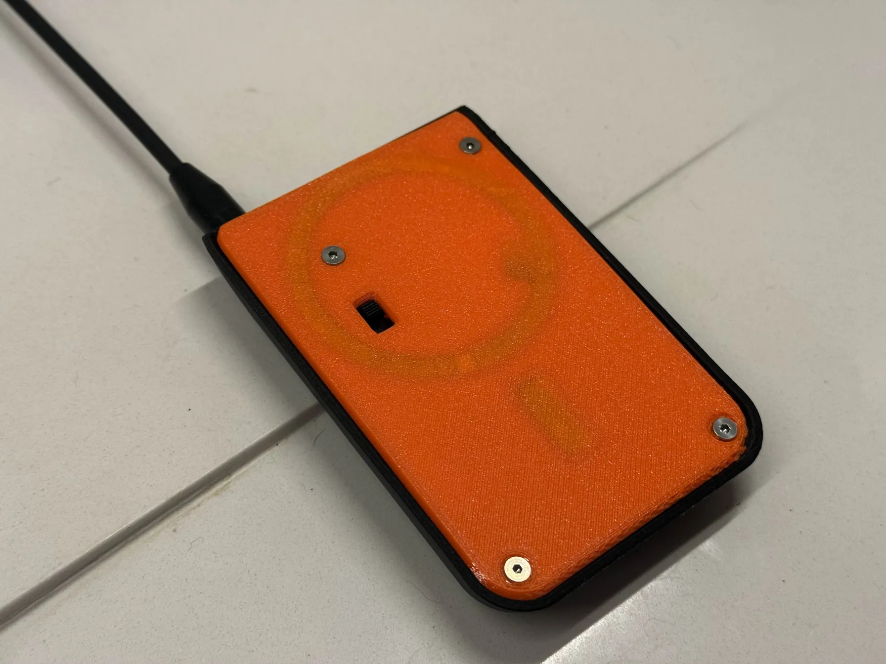 Node with orange cover with rounded edges on the back of an iPhone, with black whip antenna sticking out from top.