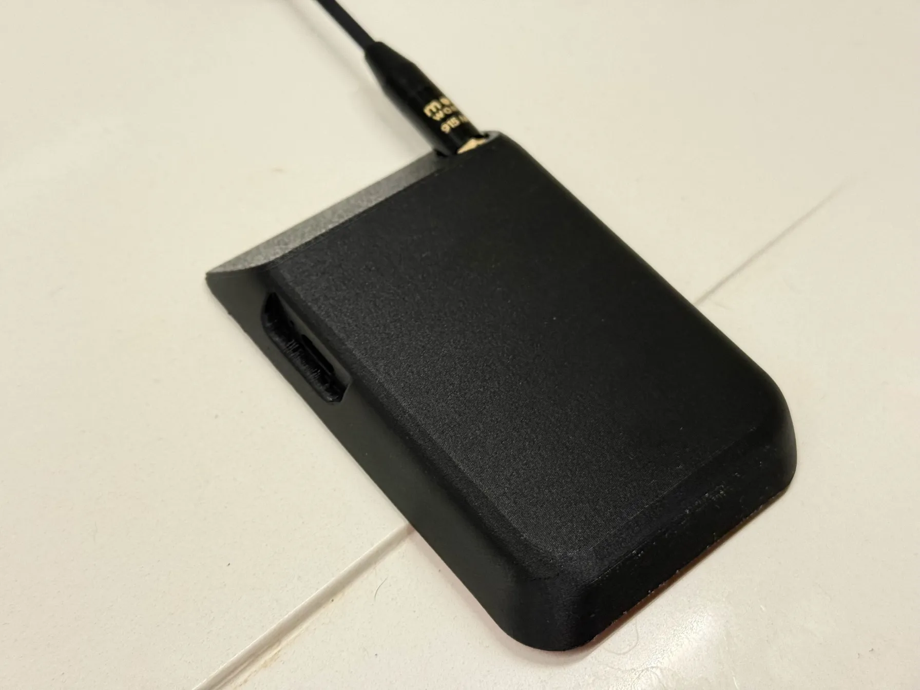Smooth matte black plastic block with rounded edges, with black whip antenna sticking out from top.
