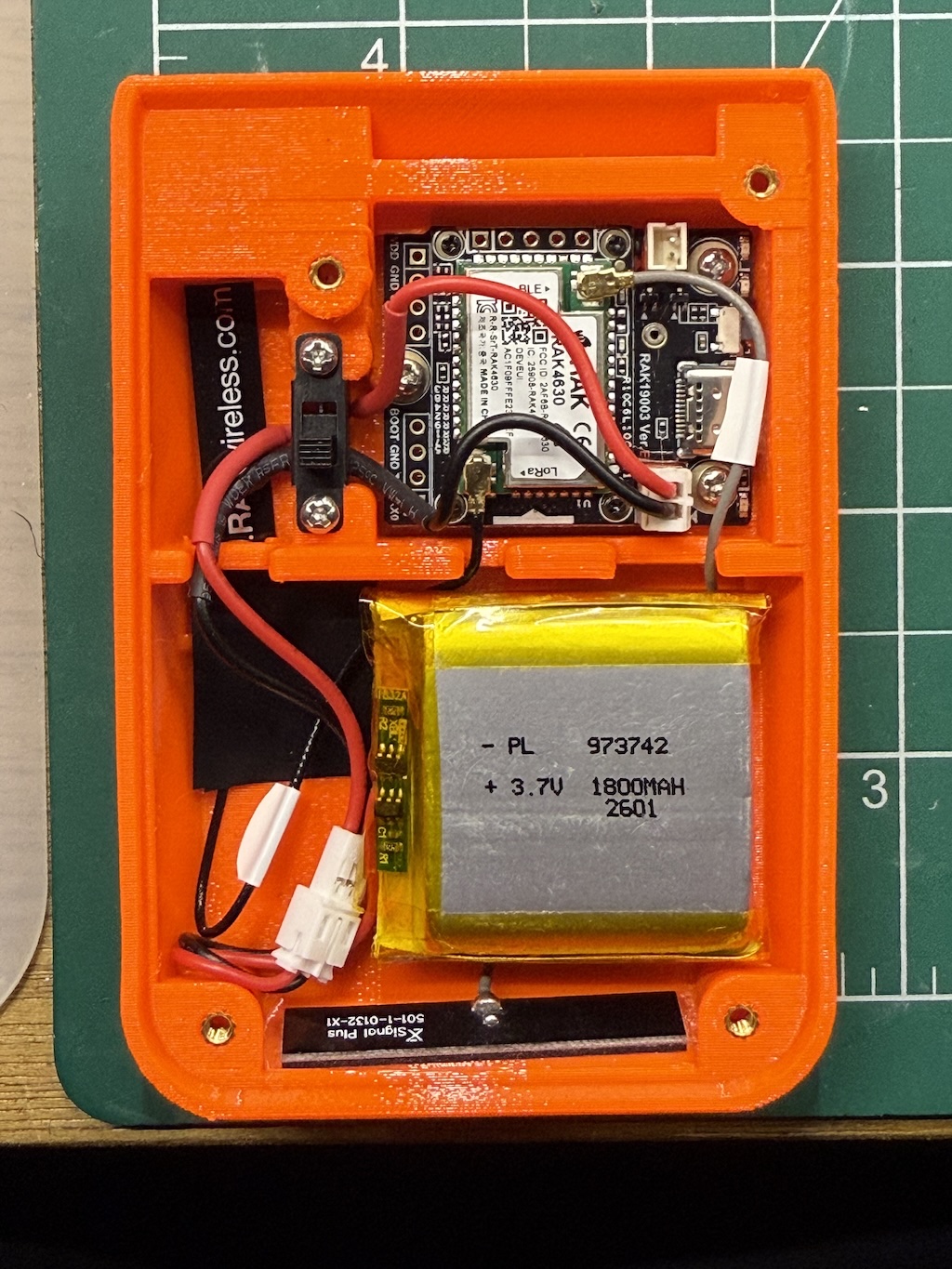 Orange plastic case with all components inserted, including battery, wires tucked into channels or cutouts.
